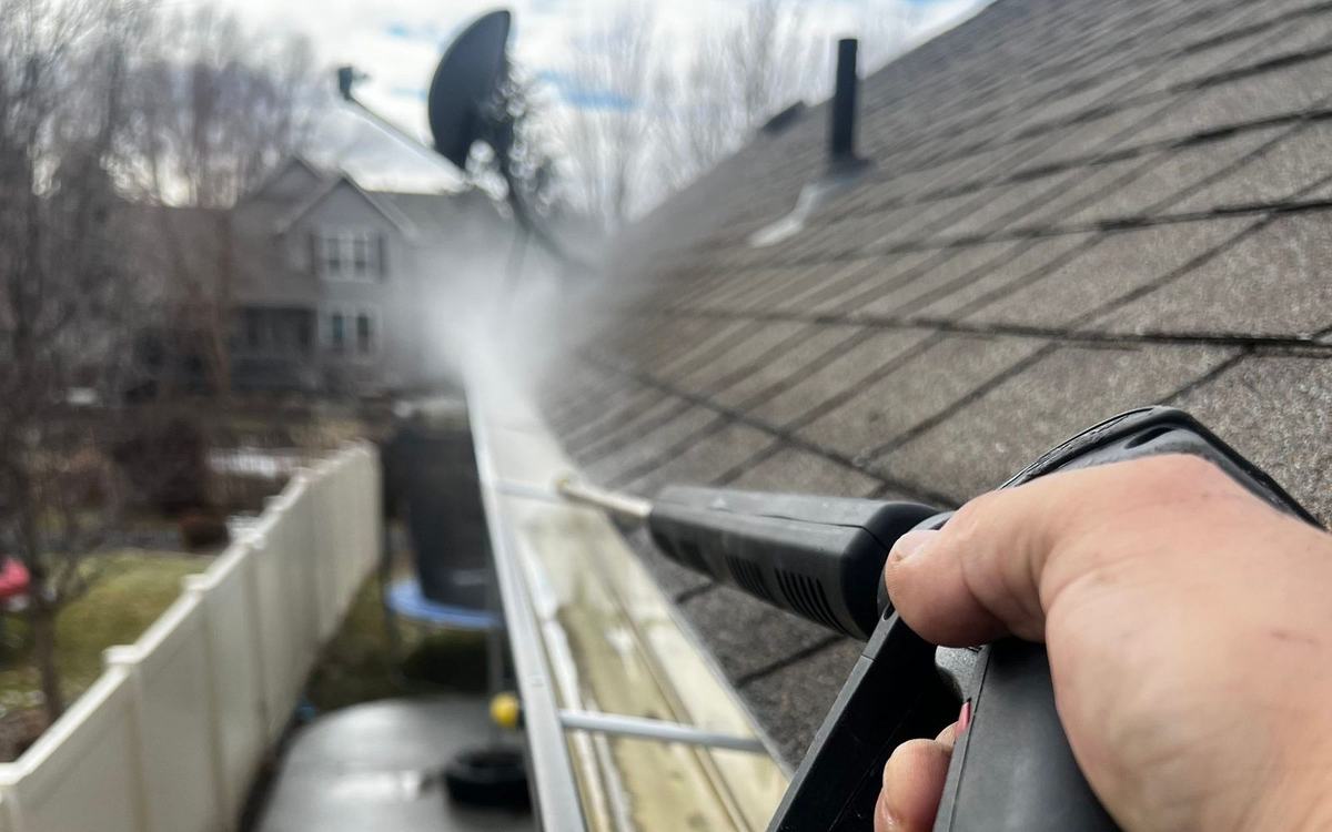 Pressure washer lance rinsing a roof gutter